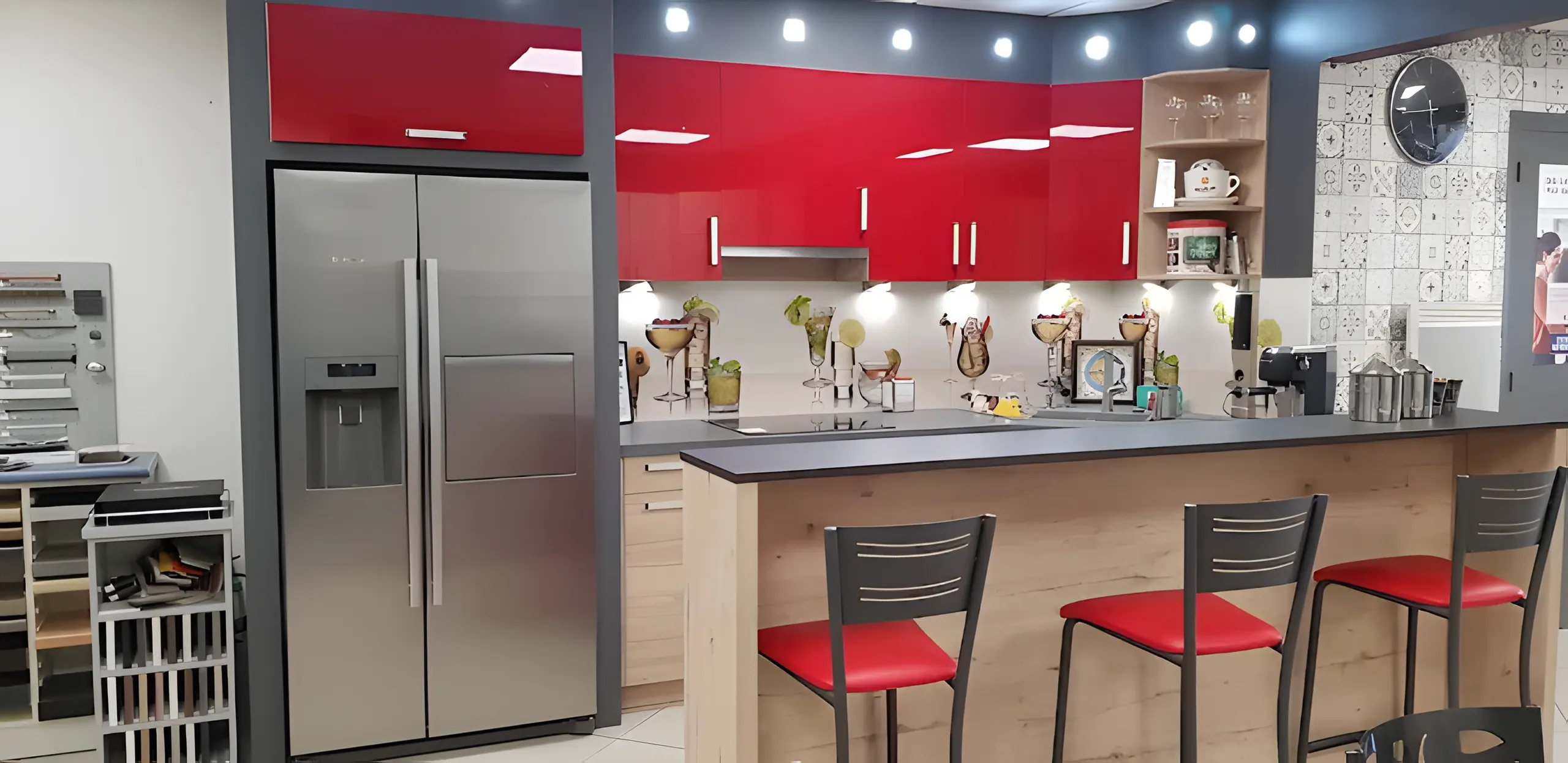 Réfrigérateur américain inox intégré à côté de la cuisine rouge du showroom, échantillons de façades à gauche