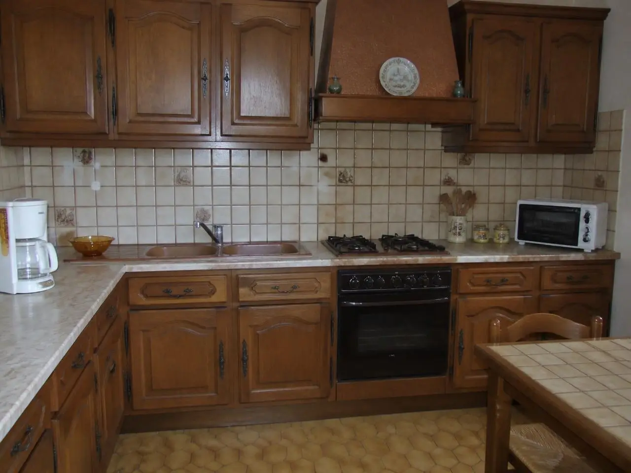 Cuisine d’angle en chêne foncé à ferrures noires, évier à deux bacs, plaque gaz et hotte cuivrée